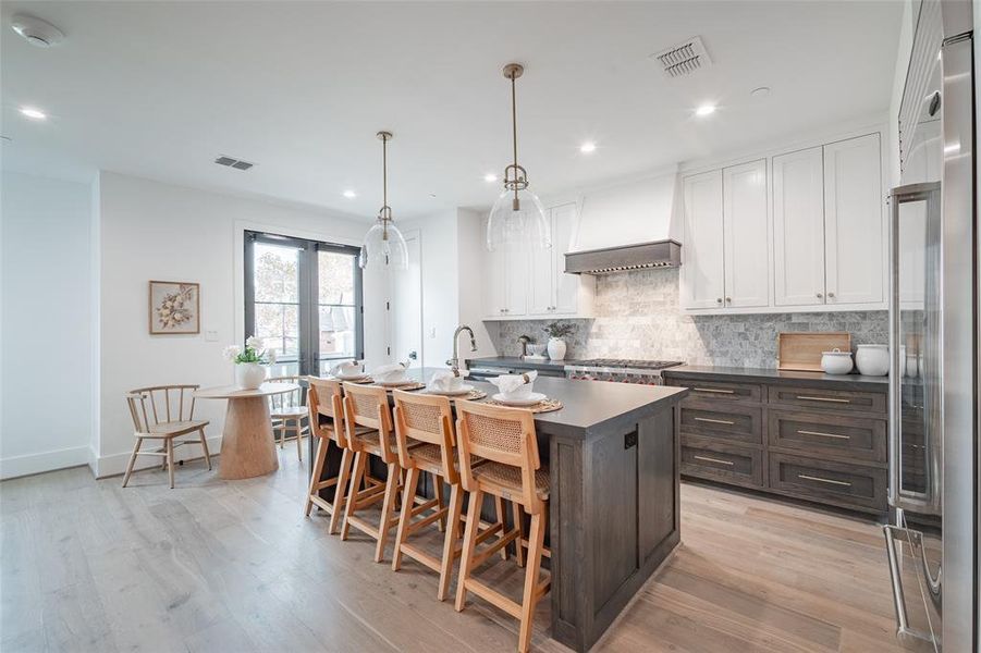 Kitchen featuring white cabinetry, light hardwood / wood-style flooring, hanging light fixtures, and custom exhaust hood