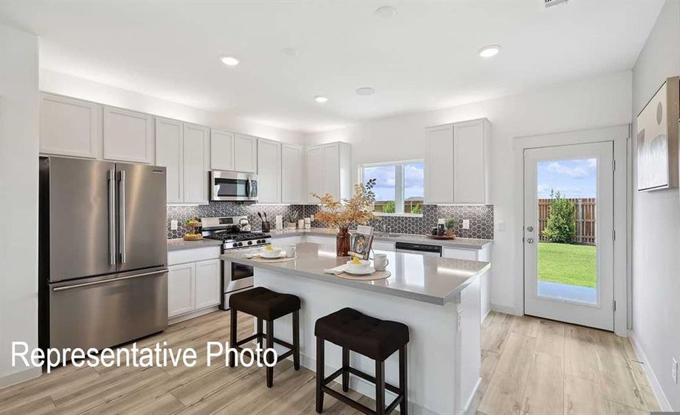 The kitchen features light-colored cabinetry, stainless steel appliances, and a central island with a light-toned countertop