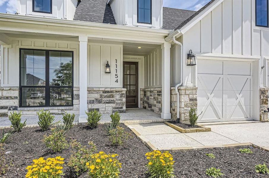 View of exterior entry featuring board and batten siding, roof with shingles, covered porch, and stone siding