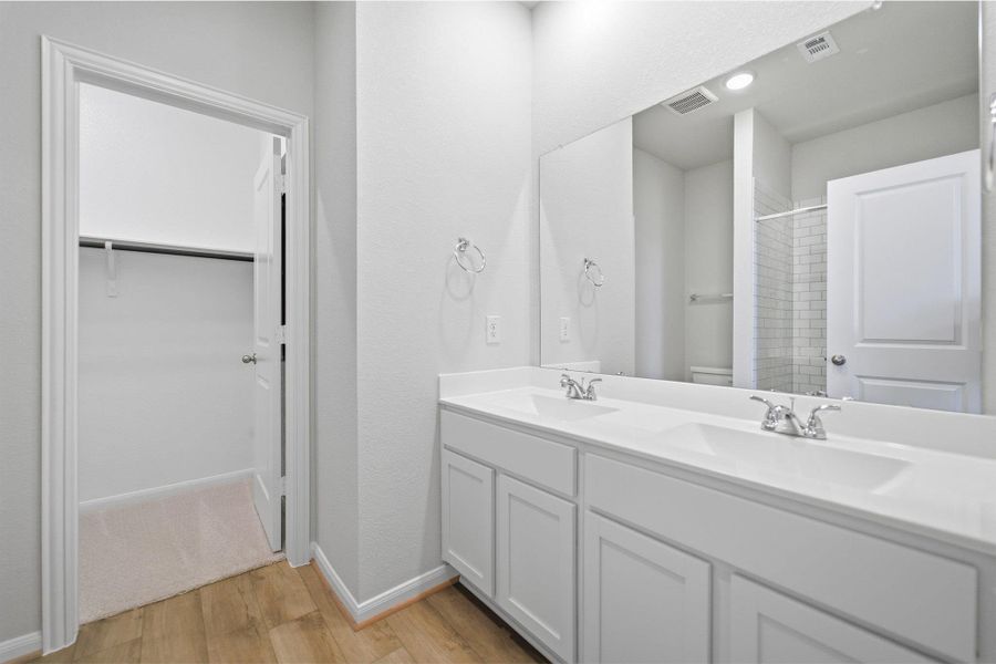 Full bath featuring double vanity, a shower stall, light wood-style floors, and a spacious closet