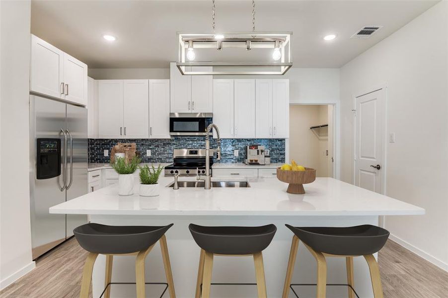 Kitchen featuring backsplash, stainless steel appliances, white cabinets, a kitchen island with sink, and a kitchen bar