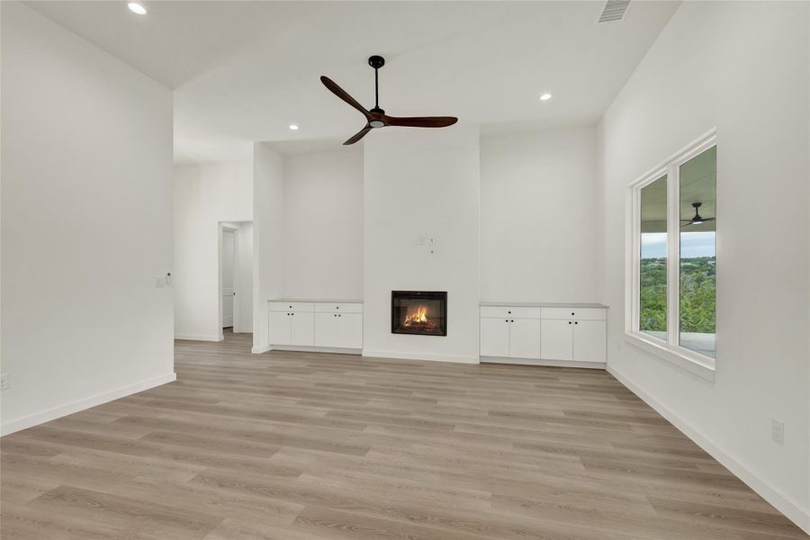 Unfurnished living room featuring a glass covered fireplace, light wood-style floors, recessed lighting, ceiling fan, and a high ceiling