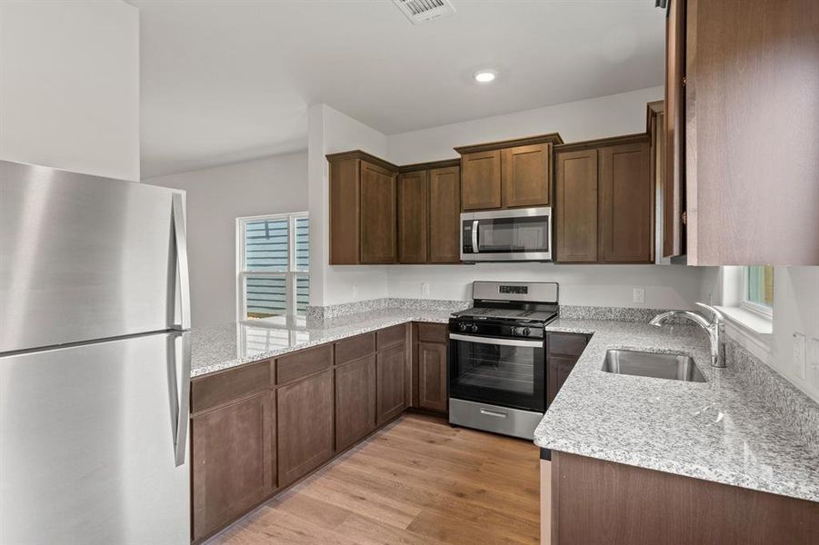 Kitchen featuring light stone countertops, appliances with stainless steel finishes, dark brown cabinetry, sink, and light hardwood / wood-style floors