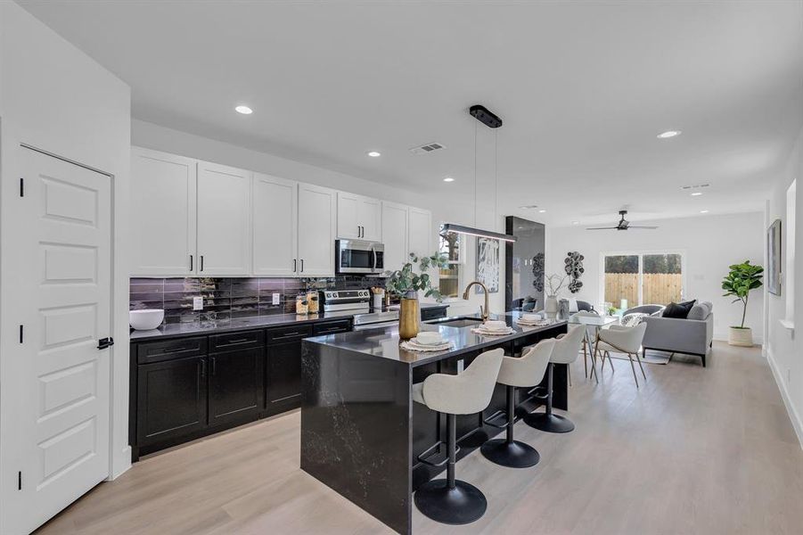 Kitchen with a kitchen island with sink, ceiling fan, decorative light fixtures, white cabinetry, and stainless steel appliances