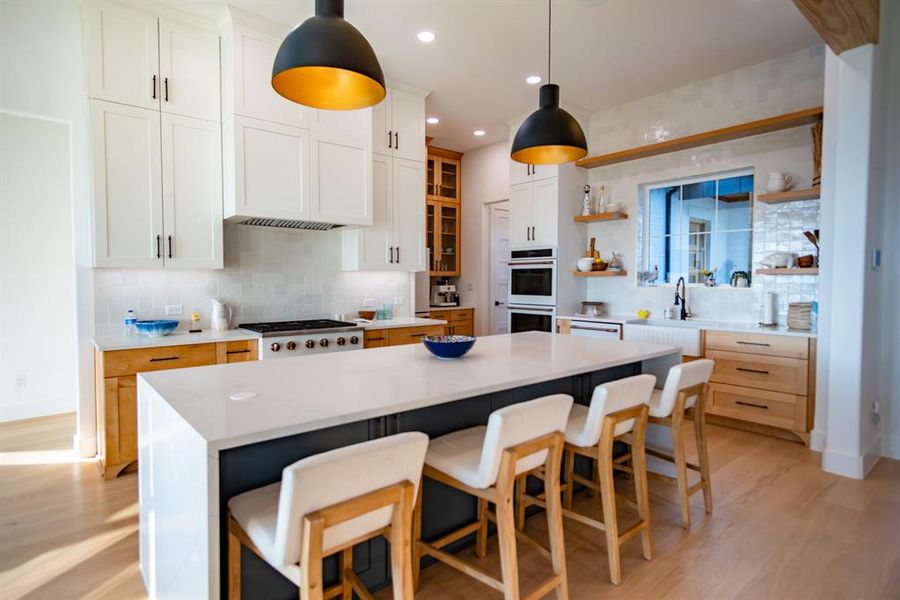 Kitchen with backsplash, white cabinets, light wood-style floors, light stone counters, and open shelves Kitchen with backsplash, white cabinets, light wood-style floors, light stone counters, and open shelves