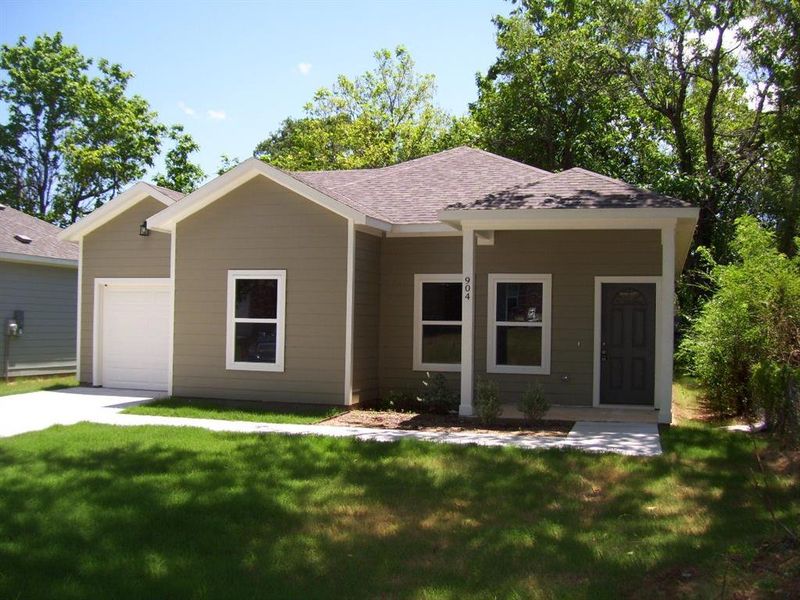Ranch-style house featuring a front lawn, a shingled roof, a garage, and driveway