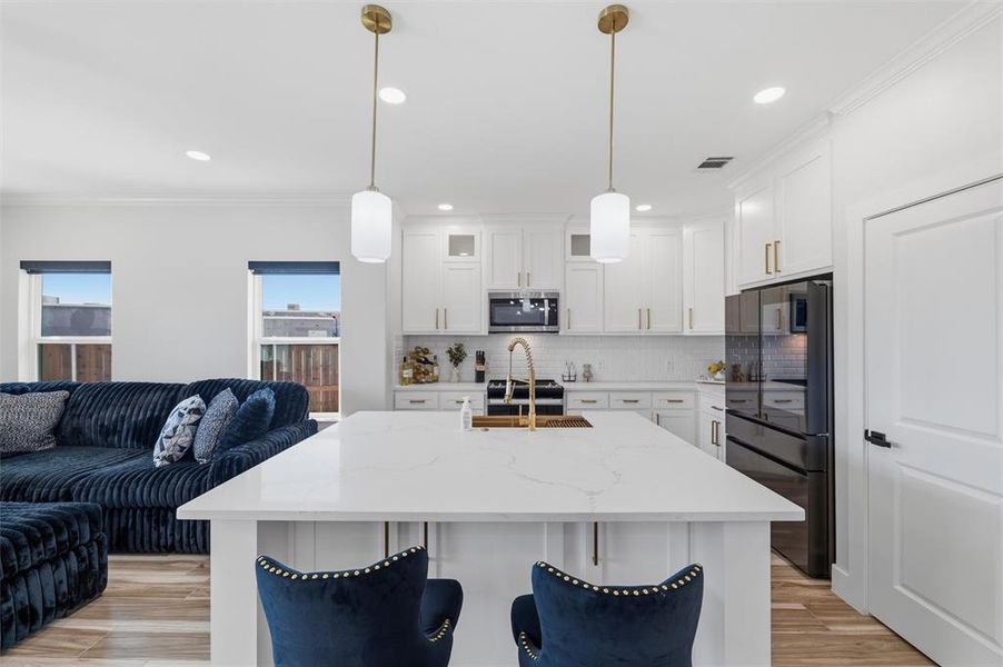 Kitchen with crown molding, a kitchen island with sink, white cabinetry, black refrigerator, and light stone counters