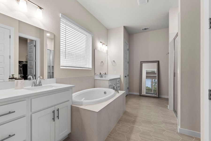Expansive bathroom featuring dual white vanities with integrated sinks, a built-in soaking tub with surrounding tile, a walk-in shower with a glass enclosure, and hexagonal wood-finish flooring