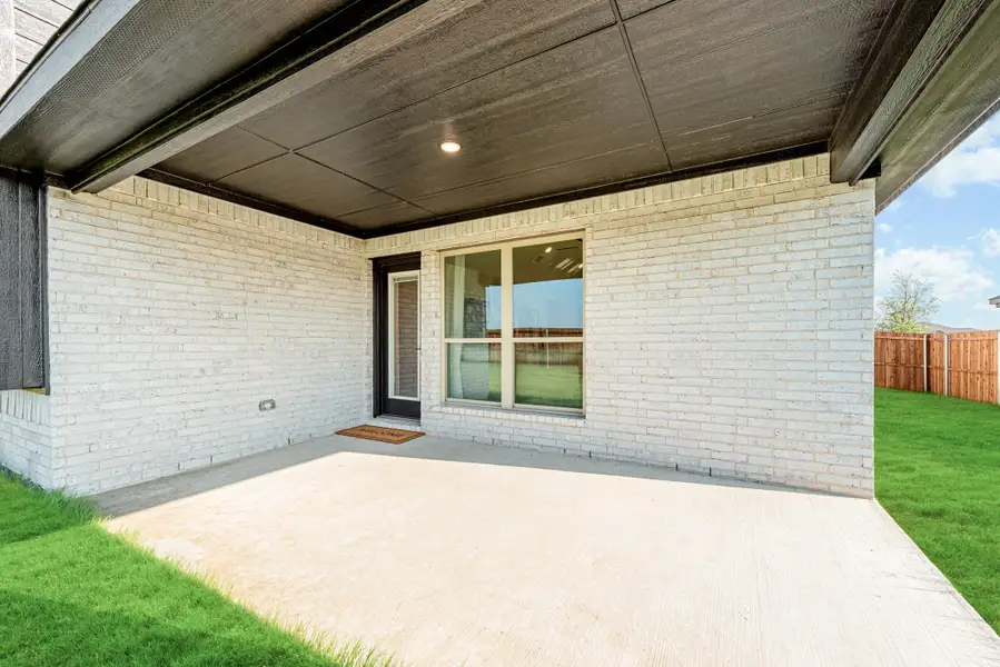 Covered back patio with concrete floor, white brick exterior, and wood privacy fence surrounding green lawn