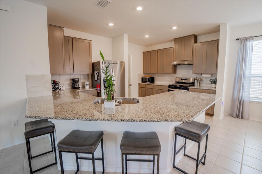 Open-concept kitchen featuring an expansive granite-finish island with integrated sink, coordinating granite-finish countertops, stainless steel appliances, and abundant cabinetry Open-concept kitchen featuring an expansive granite-finish island with integrated sink, coordinating granite-finish countertops, stainless steel appliances, and abundant cabinetry