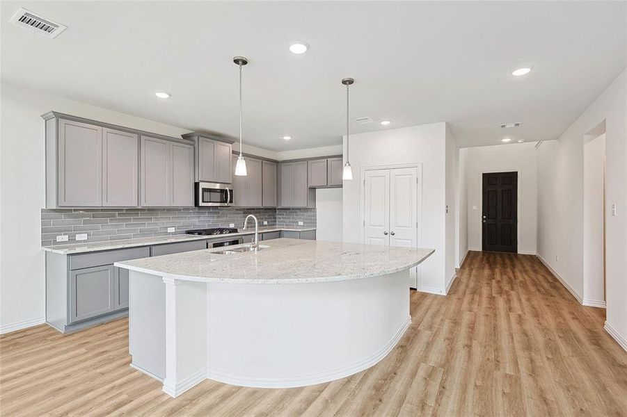 Kitchen with light stone countertops, light wood-type flooring, a kitchen island with sink, sink, and tasteful backsplash