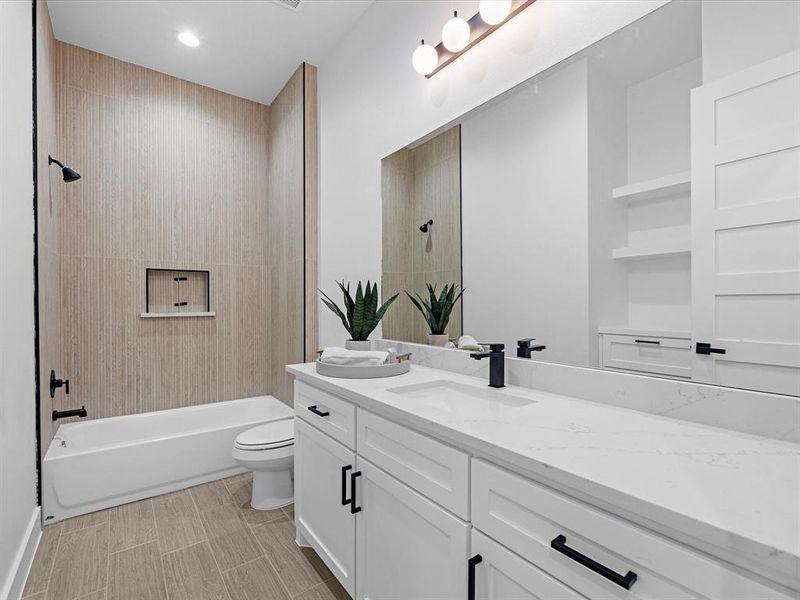 The guest bathroom is spacious, offering tons of counter space, a tub/shower combo adorned with tile finishing that extends all the way to the ceiling, complemented by black hardware.