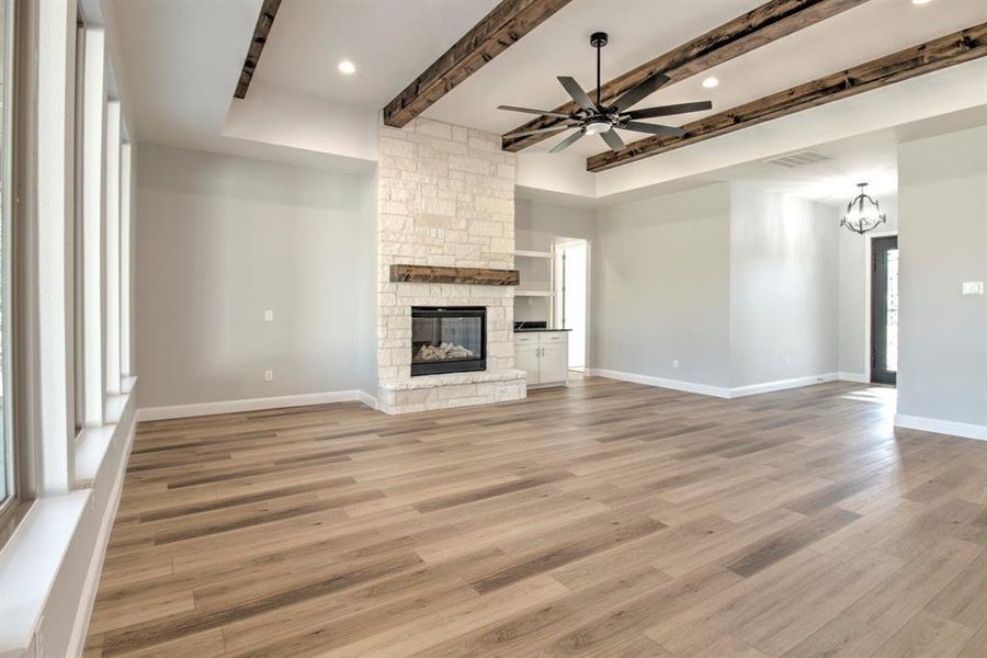 Unfurnished living room with beamed ceiling, ceiling fan with notable chandelier, light hardwood / wood-style flooring, and a fireplace