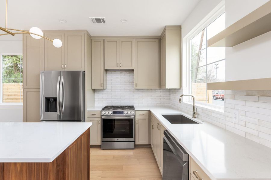 Kitchen featuring stainless steel appliances, cream cabinetry, decorative backsplash, light stone countertops, and light wood-style flooring