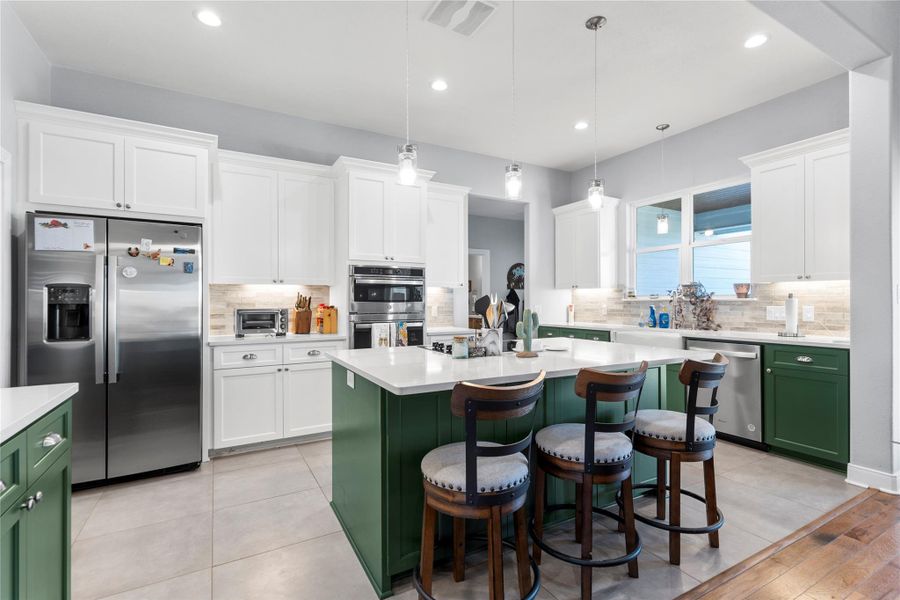 Kitchen with two tone cabinets, stainless steel appliances, a center island with sink, a kitchen bar, and pendant lighting