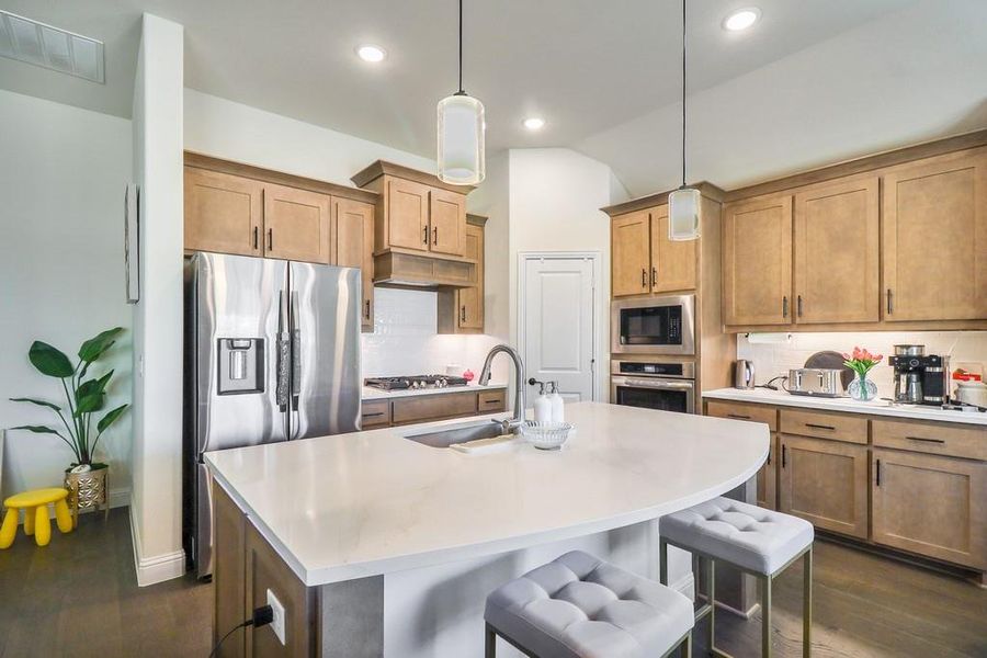 Kitchen featuring a breakfast bar, dark wood finished floors, tasteful backsplash, and stainless steel appliances Kitchen featuring a breakfast bar, dark wood finished floors, tasteful backsplash, and stainless steel appliances