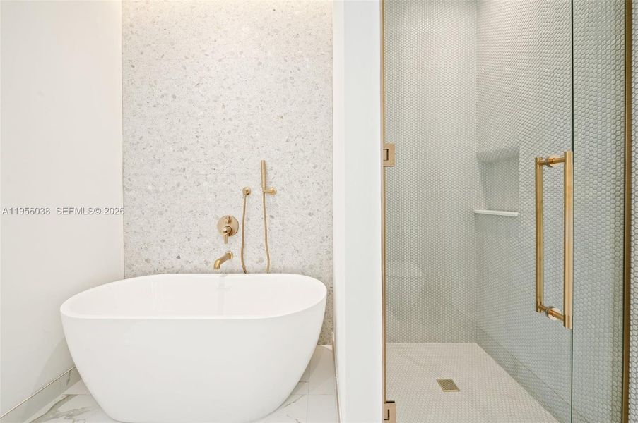 Spacious primary bathroom featuring freestanding soaking tub, glass-enclosed shower, custom vanity, and elegant designer finishes.