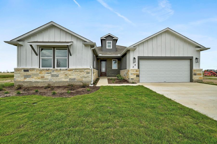 View of front facade with stone siding, board and batten siding, a garage, a front yard, and concrete driveway