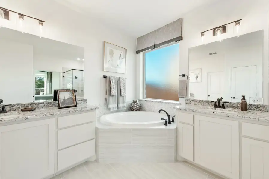 Master bathroom with dual vanities, granite countertops, and a soaking tub between white cabinets