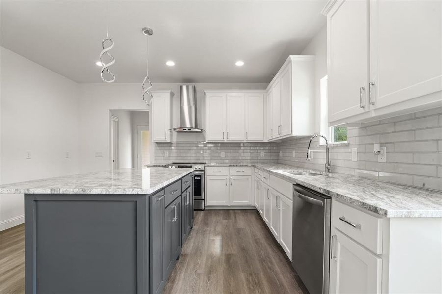Modern kitchen featuring a contrasting island with granite-style countertops, white cabinetry, a subway tile backsplash, stainless steel appliances, and wood-finish flooring