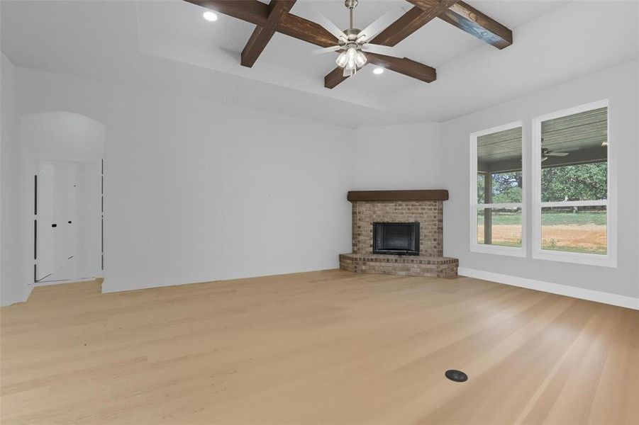 Unfurnished living room featuring light wood finished floors, a brick fireplace, coffered ceiling, ceiling fan, and beamed ceiling Unfurnished living room featuring light wood finished floors, a brick fireplace, coffered ceiling, ceiling fan, and beamed ceiling