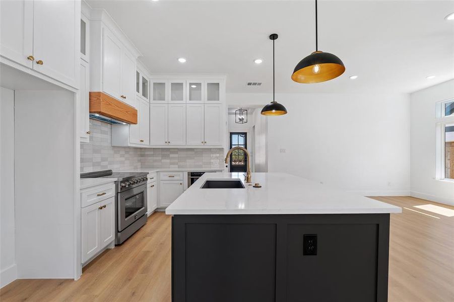 Kitchen with high end stainless steel range oven, light hardwood / wood-style floors, sink, white cabinetry, and decorative light fixtures