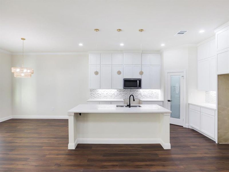 Kitchen featuring decorative backsplash, white cabinetry, dark wood-type flooring, pendant lighting, and ornamental molding Kitchen featuring decorative backsplash, white cabinetry, dark wood-type flooring, pendant lighting, and ornamental molding