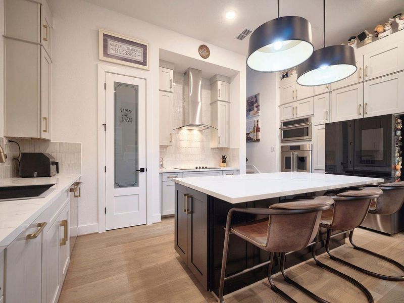 The chef's kitchen boasts a spacious island with seating, elegant pendant lighting, a built-in oven, and a custom glass-door pantry. A second staircase conveniently leads to the game and movie rooms.