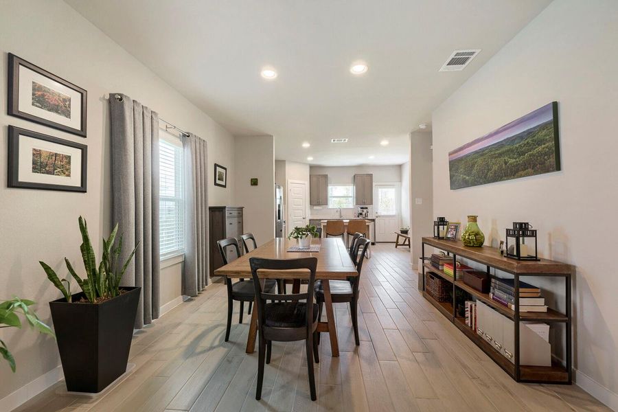 An open-concept living area with a dining table and kitchen beyond, features recessed lighting and light-toned flooring. An open-concept living area with a dining table and kitchen beyond, features recessed lighting and light-toned flooring.