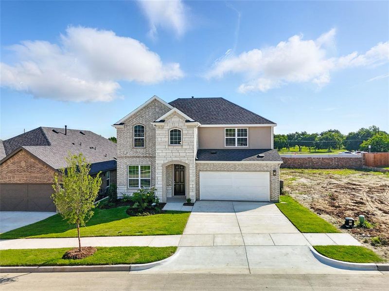 French country inspired facade featuring concrete driveway, stone siding, a front lawn, roof with shingles, and an attached garage French country inspired facade featuring concrete driveway, stone siding, a front lawn, roof with shingles, and an attached garage