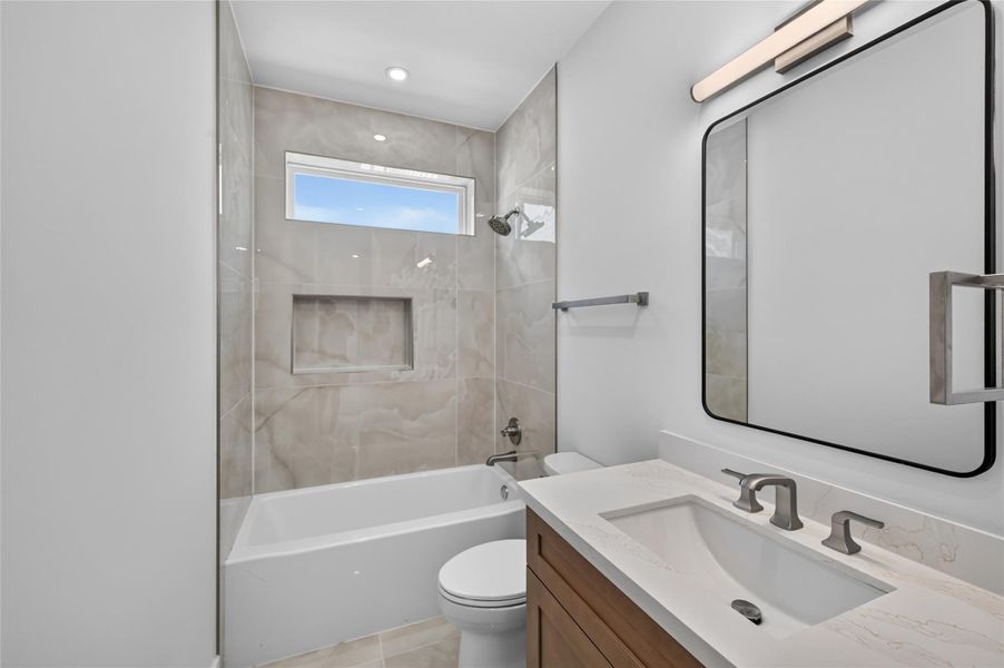 Secondary bathroom with custom cabinet and beautiful creamy colored tile that extends to the ceiling.