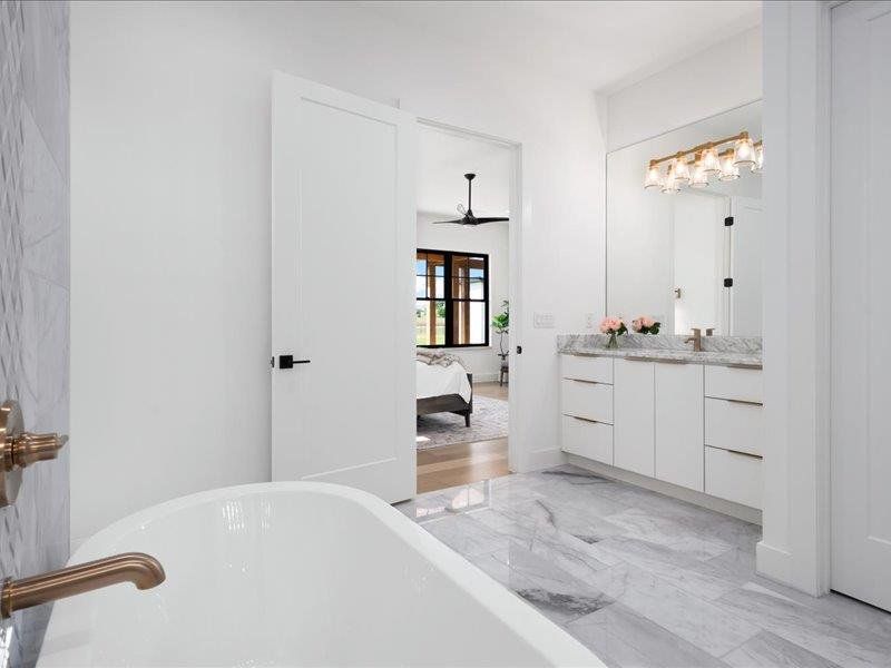 Ensuite bathroom featuring a freestanding bath, vanity, a ceiling fan, and marble finish flooring