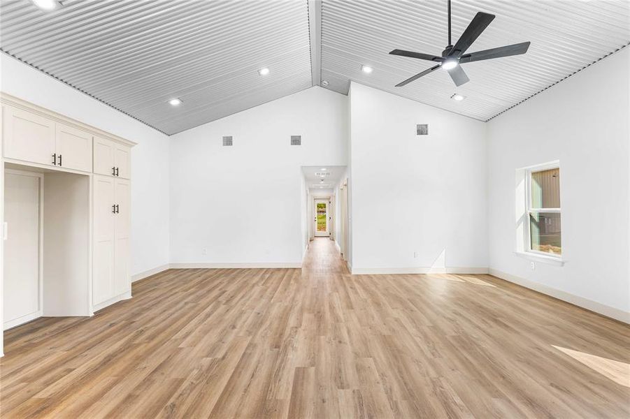 Unfurnished living room with light wood-type flooring, high vaulted ceiling, recessed lighting, and a ceiling fan Unfurnished living room with light wood-type flooring, high vaulted ceiling, recessed lighting, and a ceiling fan