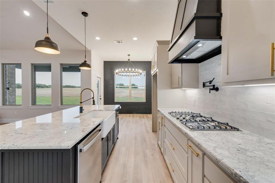 Kitchen with light stone counters, decorative light fixtures, white cabinets, light wood finished floors, and decorative backsplash Kitchen with light stone counters, decorative light fixtures, white cabinets, light wood finished floors, and decorative backsplash