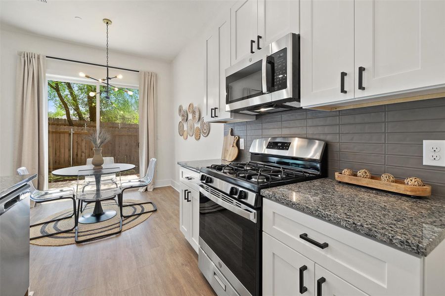 Kitchen featuring stainless steel appliances, backsplash, dark stone counters, white cabinets, and light wood-type flooring Kitchen featuring stainless steel appliances, backsplash, dark stone counters, white cabinets, and light wood-type flooring