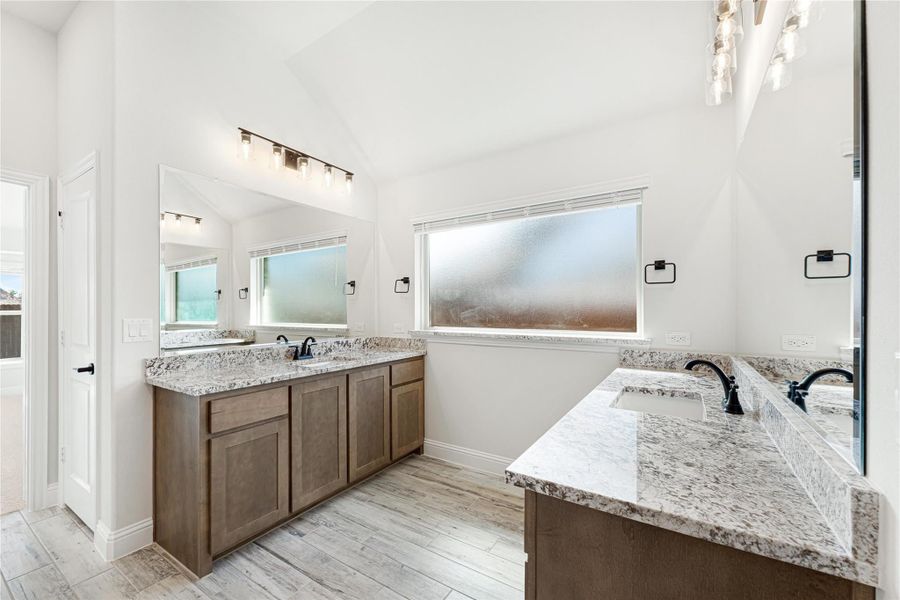 Bathroom with dual vanities, granite countertops, wood cabinets, and vaulted ceiling with frosted window