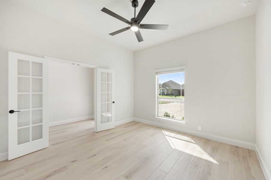 Empty bedroom with light wood floors, ceiling fan, and French doors leading to adjacent room