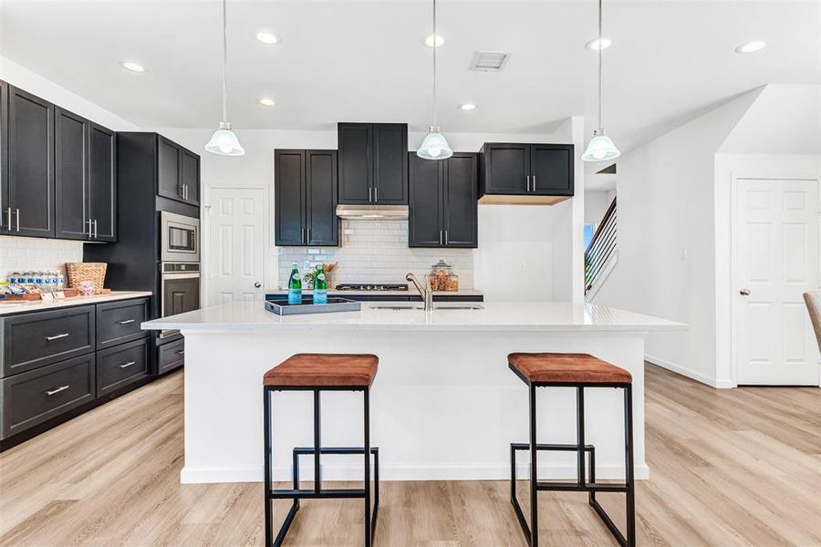 Kitchen with backsplash, decorative light fixtures, and light wood-type flooring