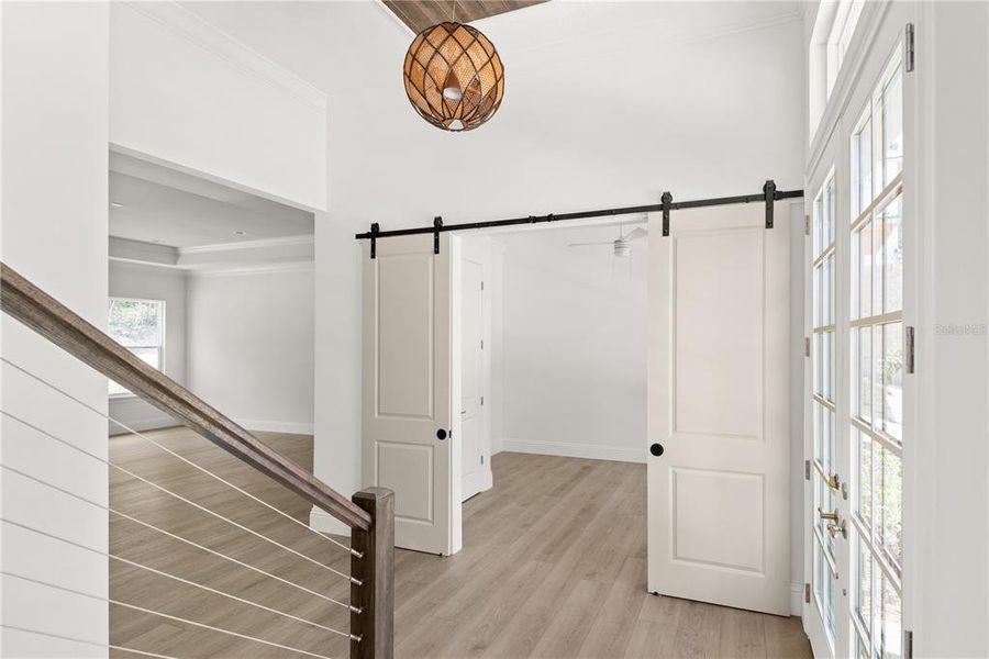 View from the foyer showcasing the office entrance, highlighted by sliding barn doors, with a glimpse into the adjacent room and its ample natural light.