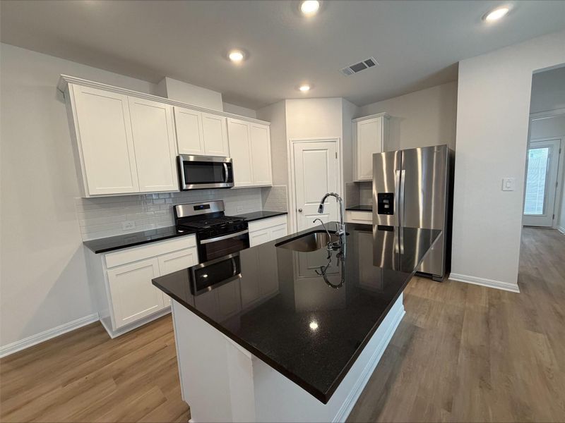 Kitchen featuring decorative backsplash, appliances with stainless steel finishes, white cabinetry, a kitchen island with sink, and light wood-style floors