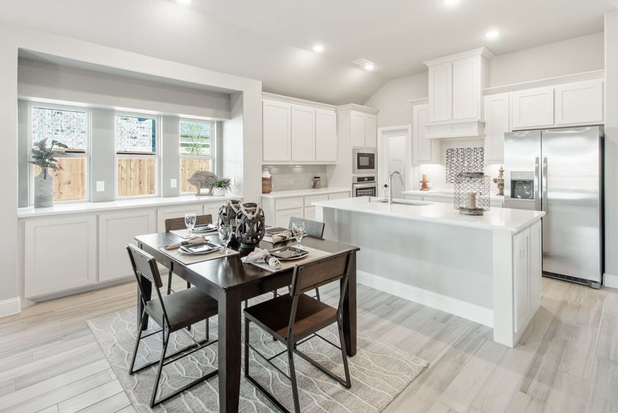 Open kitchen and dining area with white cabinets, large island, stainless appliances, and light wood floors