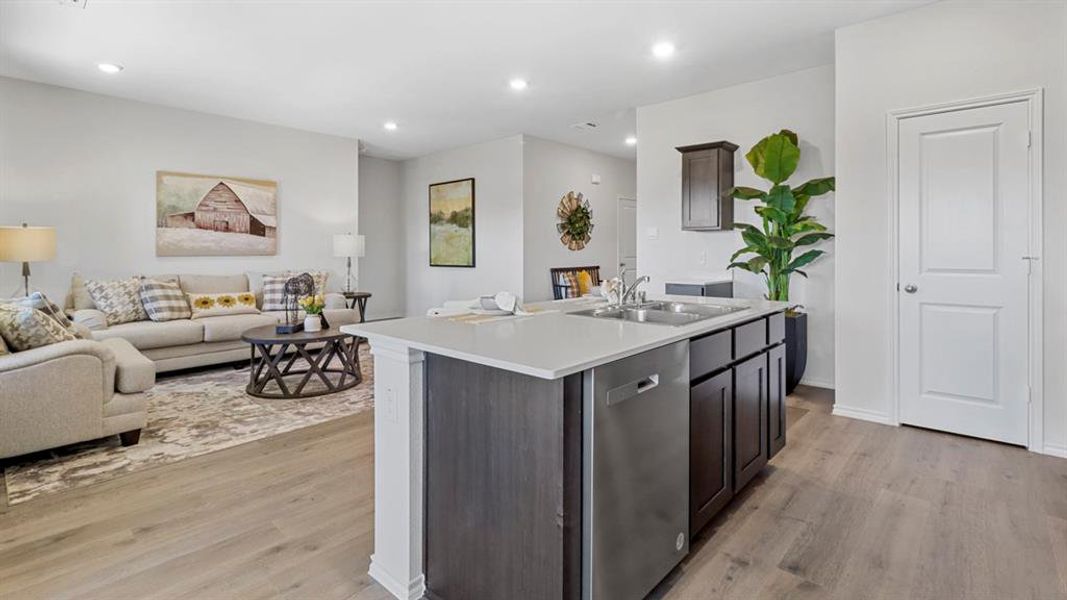 Kitchen featuring open floor plan, light countertops, dishwasher, dark wood finish cabinets, and a center island with sink