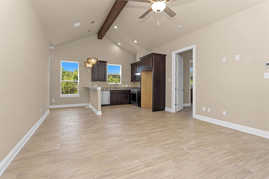 The guest home's open living area features vaulted ceilings with a rustic beam, rich cabinetry, full kitchen, and large windows framing peaceful wooded views.