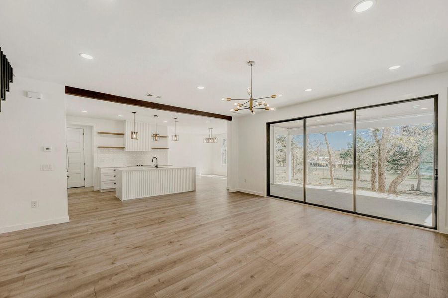 Unfurnished living room with beam ceiling, suspended lighting, and light wood-type flooring