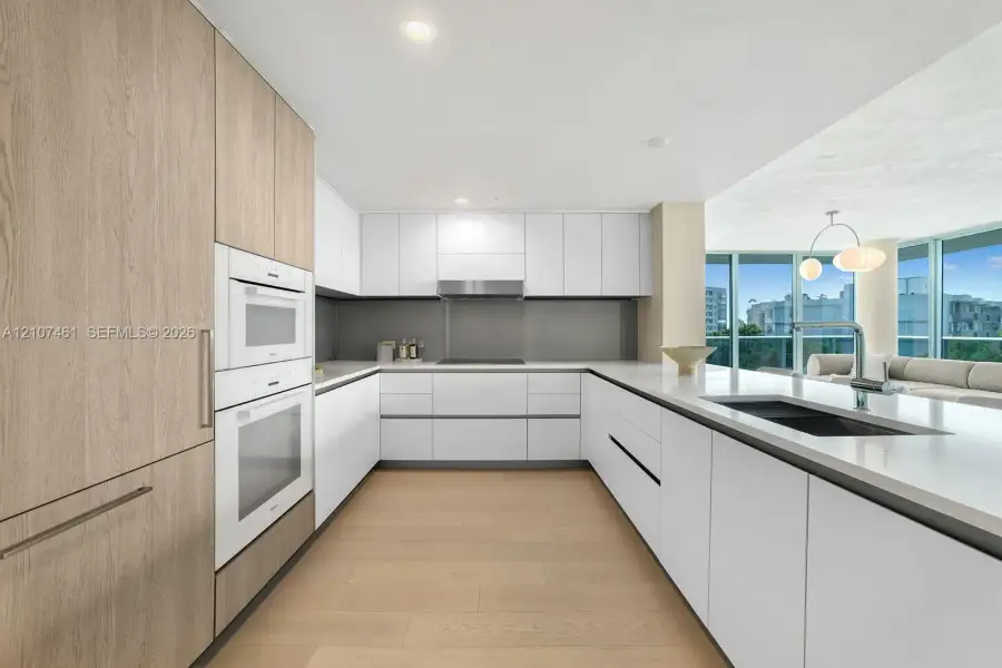 Modern kitchen featuring flat-panel cabinetry, light-toned wood-finish flooring, integrated wall ovens, solid-surface countertops, and recessed lighting Modern kitchen featuring flat-panel cabinetry, light-toned wood-finish flooring, integrated wall ovens, solid-surface countertops, and recessed lighting