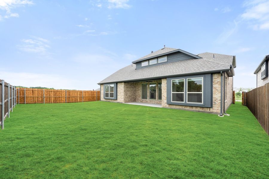 Rear view of brick home with large fenced backyard, gray trim windows, and covered patio area