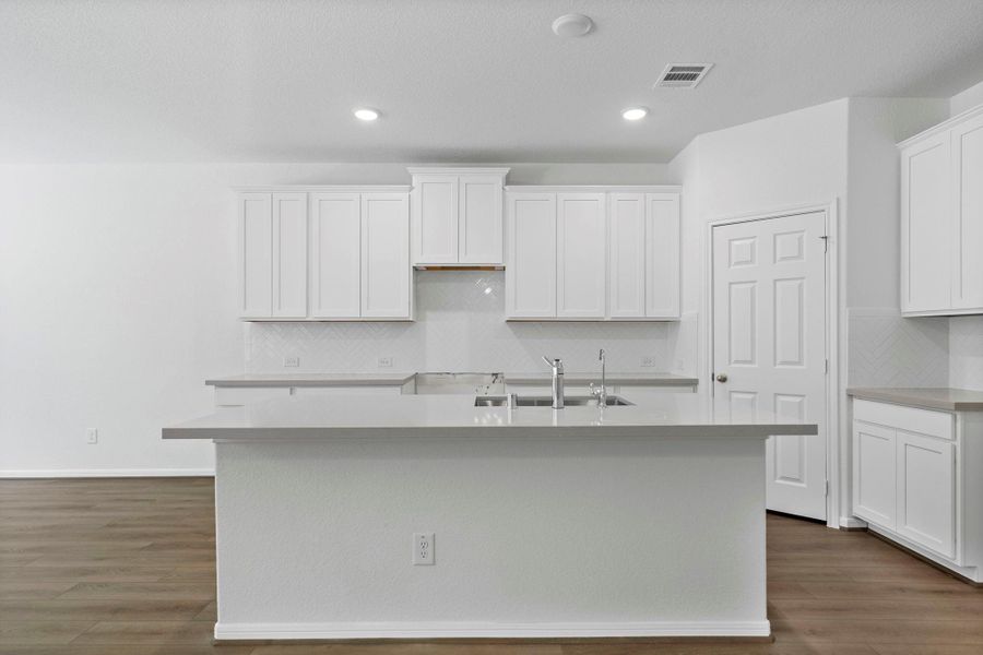 This light and bright kitchen features a large quartz island, white cabinets, a large sink overlooking your family room, recessed lighting, and beautiful backsplash. This light and bright kitchen features a large quartz island, white cabinets, a large sink overlooking your family room, recessed lighting, and beautiful backsplash.