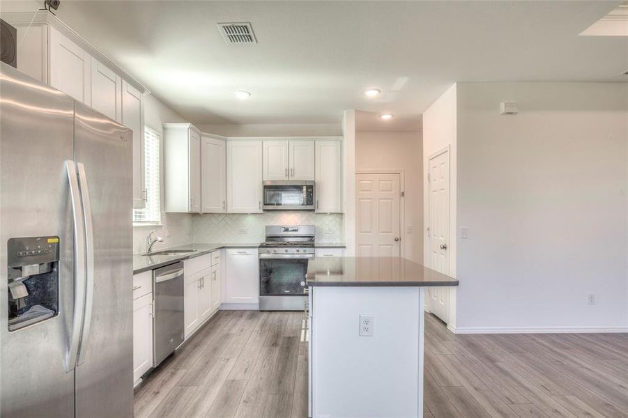 Kitchen appliances with stainless steel finishes, white cabinets, decorative backsplash, a center island, and recessed lighting Kitchen appliances with stainless steel finishes, white cabinets, decorative backsplash, a center island, and recessed lighting