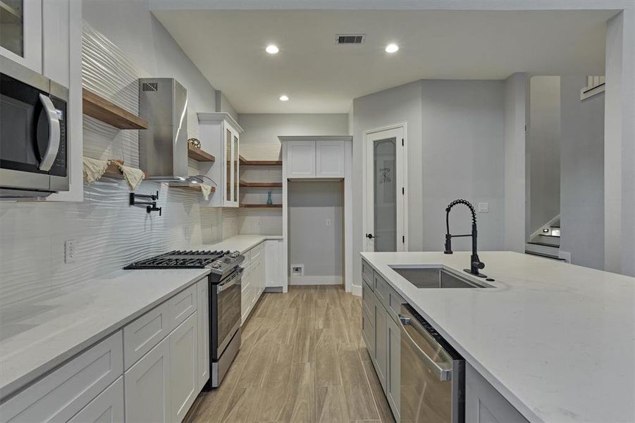 Designer backsplash extends to the top of the cabinets. A corner walk-in pantry is just beyond.