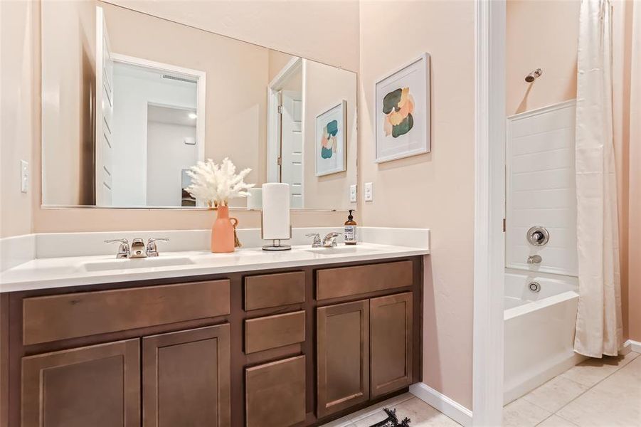 Bathroom with shower / bathtub combination with curtain, light tile patterned floors, and double vanity